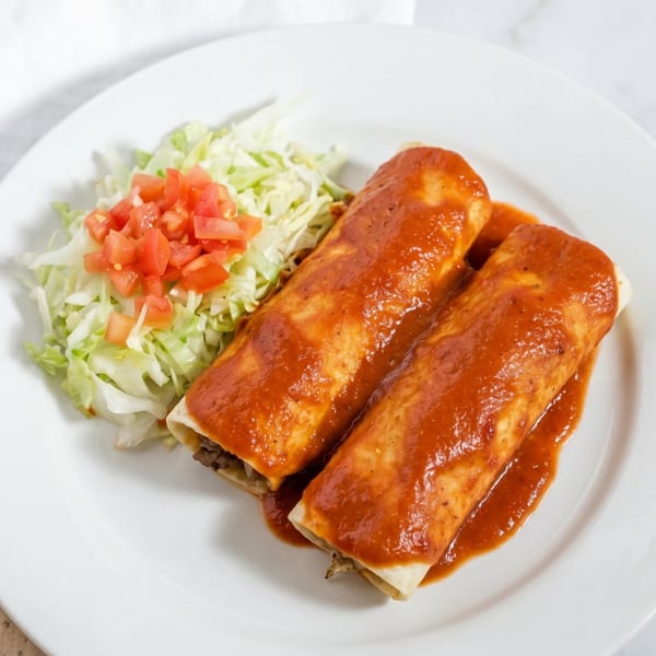 Two enchiladas covered in red sauce, with a side of shredded lettuce and diced tomatoes.