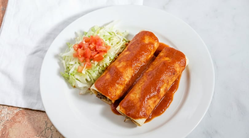 Two enchiladas covered in red sauce, with a side of shredded lettuce and diced tomatoes.