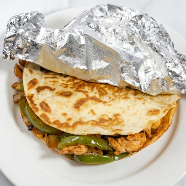Chicken fajita quesadilla with green peppers and onions, partially wrapped in foil on a white plate.