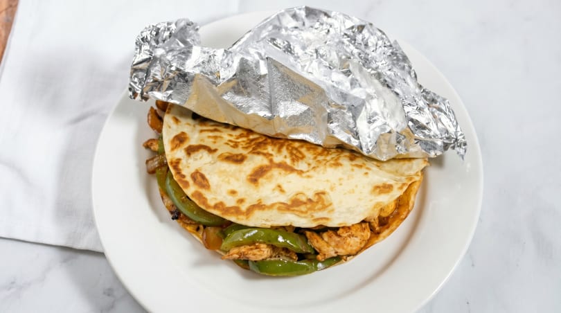 Chicken fajita quesadilla with green peppers and onions, partially wrapped in foil on a white plate.