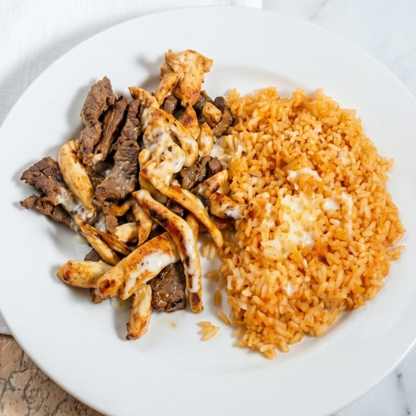 A white plate with grilled chicken and steak strips, and a side of orange rice.