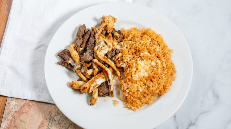 A white plate with grilled chicken and steak strips, and a side of orange rice.
