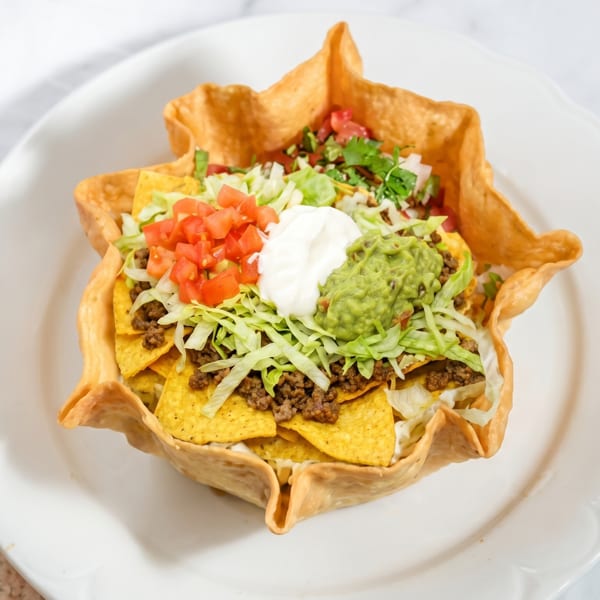 Taco salad in a crispy tortilla bowl, topped with ground beef, lettuce, tomatoes, sour cream, and guacamole.