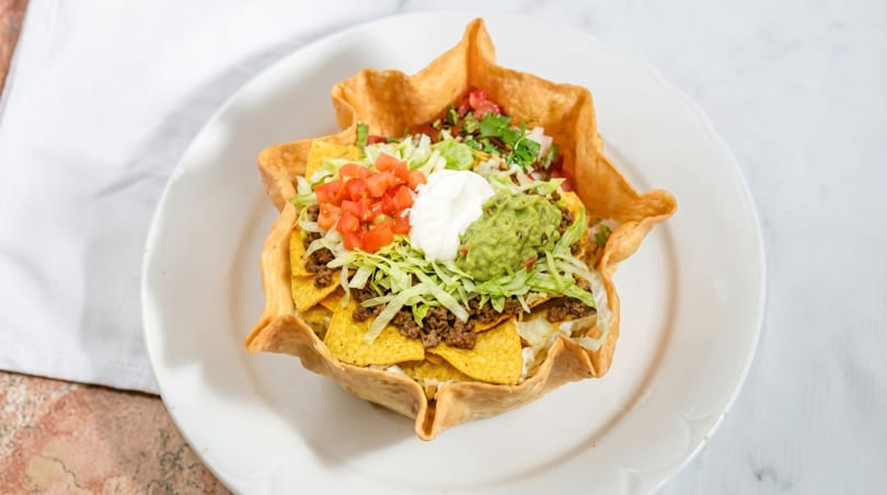 Taco salad in a crispy tortilla bowl, topped with ground beef, lettuce, tomatoes, sour cream, and guacamole.