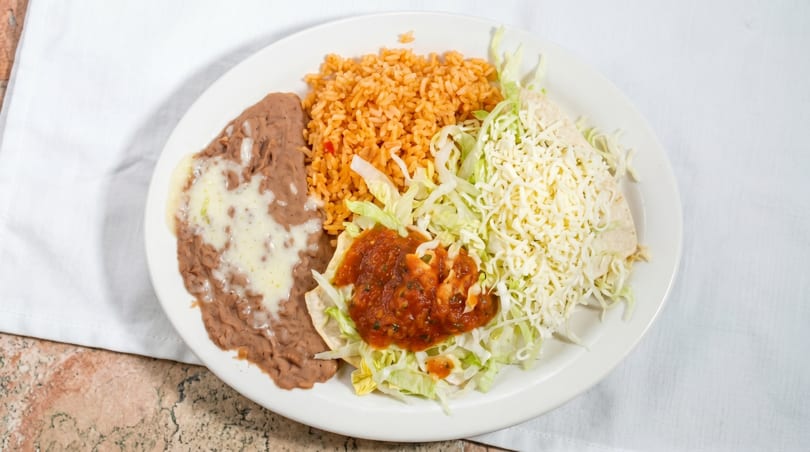 A white plate with refried beans, rice, shredded lettuce, salsa, and a cheese-covered tortilla.