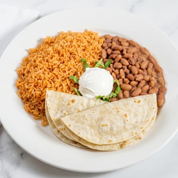 Mexican rice, pinto beans, flour tortillas, and a dollop of sour cream with cilantro.